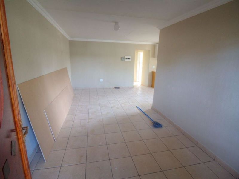 An empty, open-plan living area featuring neutral ceramic floor tiles and coved ceiling cornices, presenting a blank canvas for potential interior design updates.