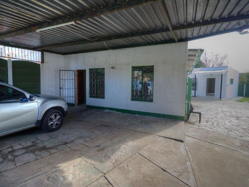 A covered carport area with a concrete driveway and paved courtyard, featuring security gates and bars on the building exterior.