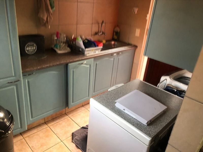A compact scullery area featuring built-in cabinetry, a stainless steel sink, and tiled finishes, providing functional utility space for the apartment.
