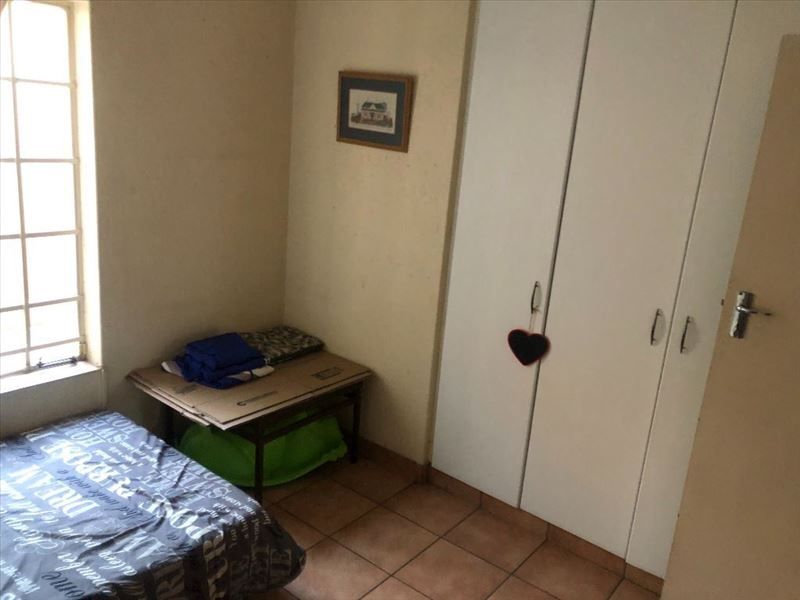 A bedroom featuring tiled flooring, built-in cupboards, and a window with security bars. The room requires cosmetic updates to improve its overall condition.