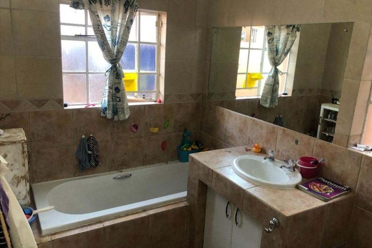 A functional bathroom featuring a built-in bathtub, tiled vanity with drop-in basin, and a large wall mirror, finished with neutral wall tiling.