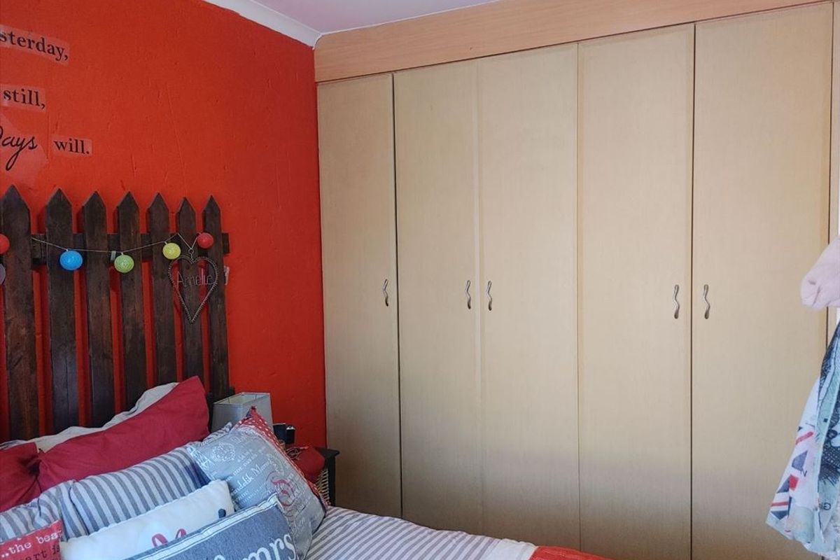 A bedroom featuring floor-to-ceiling built-in cupboards with a neutral finish and a bold red accent wall.