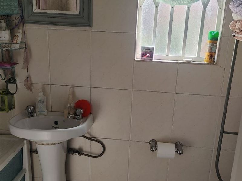 A compact bathroom featuring a pedestal basin, toilet, and tiled finishes, requiring some maintenance and cosmetic updates.
