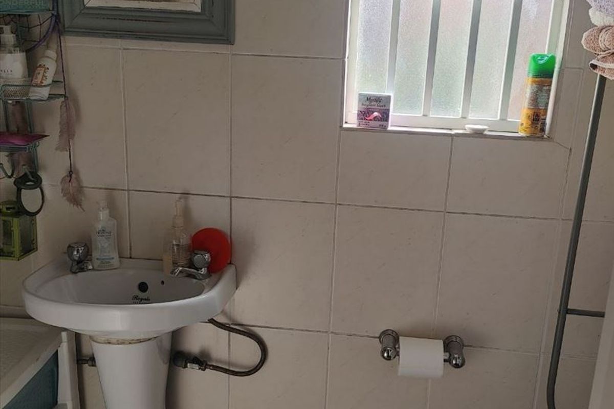 A compact bathroom featuring a pedestal basin, toilet, and tiled finishes, requiring some maintenance and cosmetic updates.