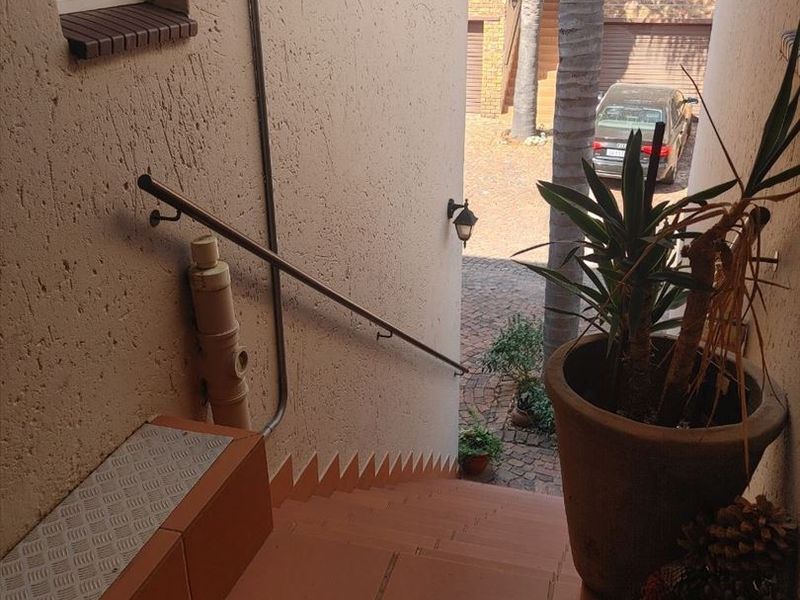 An exterior staircase with tiled steps and a metal handrail leading down towards a paved driveway area.