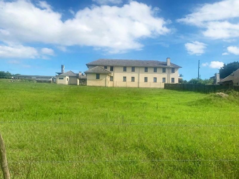A view of the rear elevation of a large residential building set within a spacious, grassy field enclosed by a wire fence.