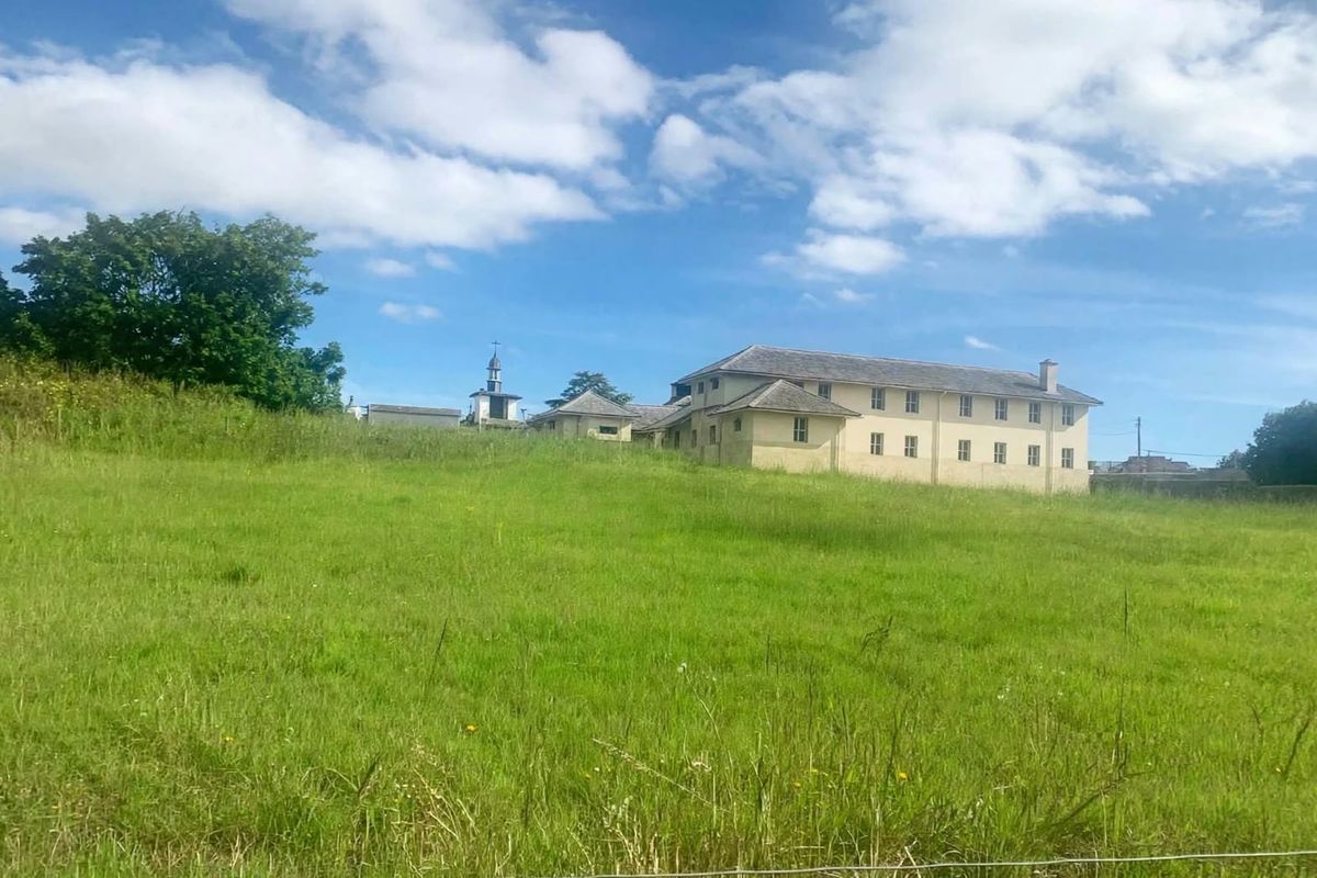 A view of a large multi-story building situated on a sloped, grassy residential plot.