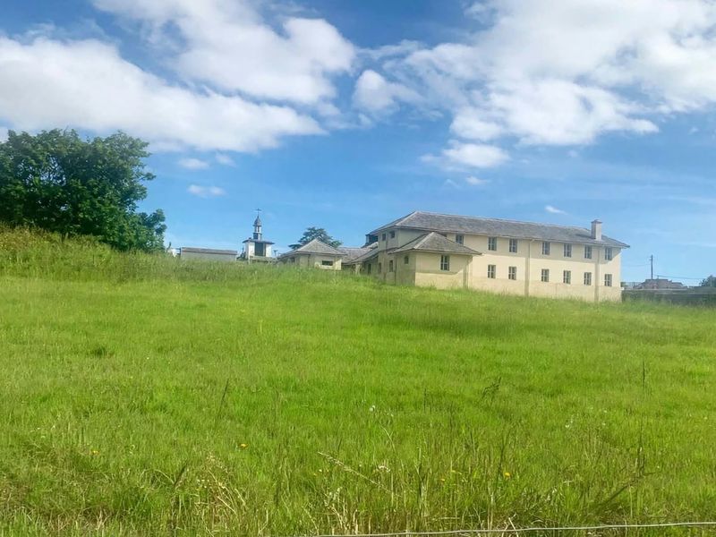 A view of a large multi-story building situated on a sloped, grassy residential plot.