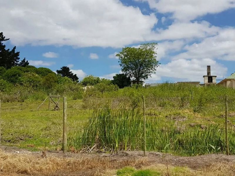 A view of a vacant residential plot featuring wire fencing and established vegetation with a neighboring building visible in the background.
