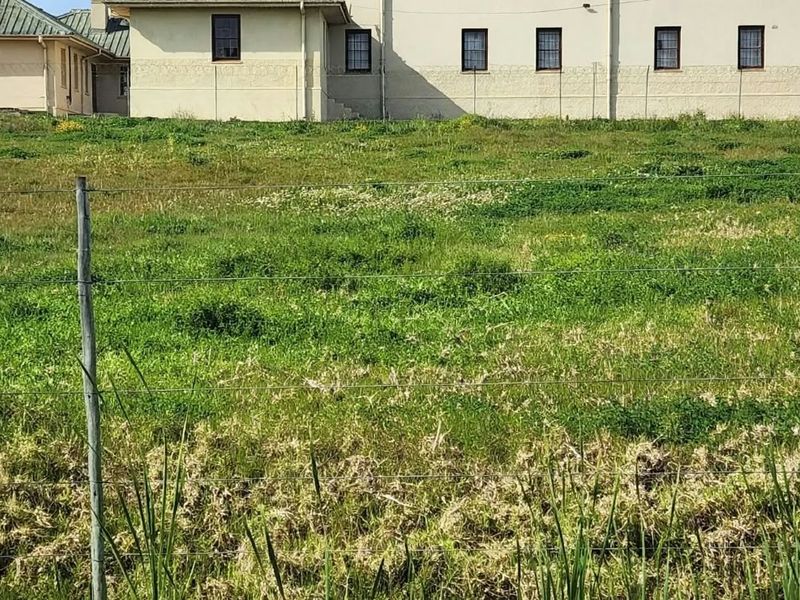 A view of a vacant residential plot featuring a wire fence boundary and a view of the adjacent building's rear facade.