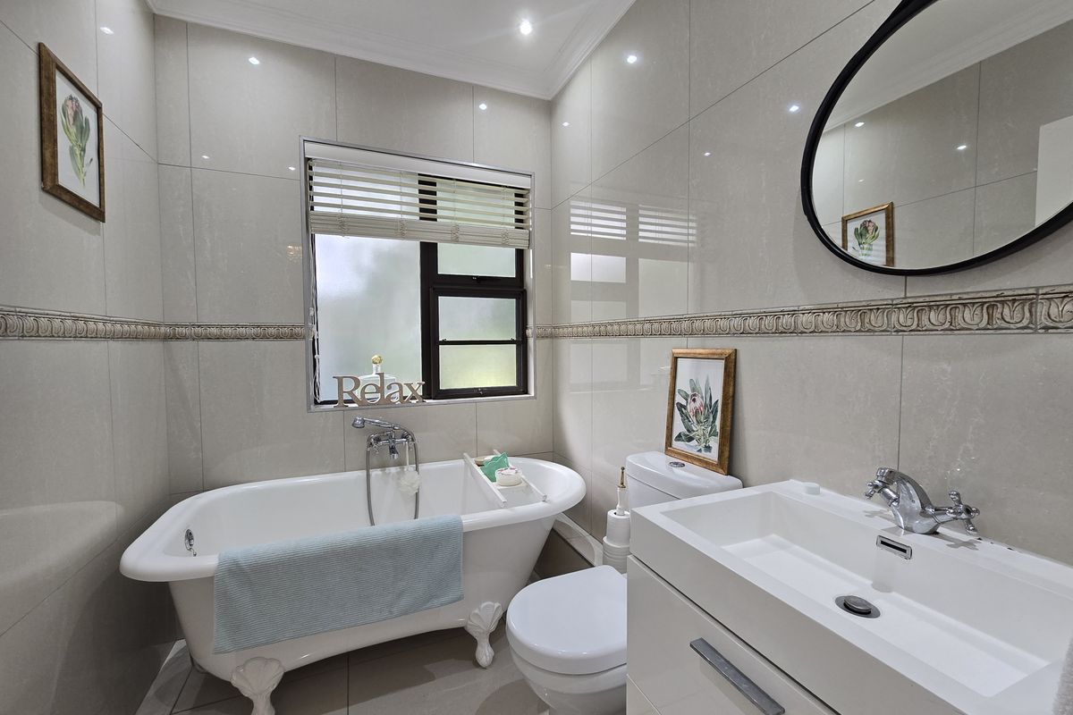 A well-maintained bathroom featuring a classic freestanding bathtub, modern vanity with basin, toilet, and neutral floor-to-ceiling wall tiles.