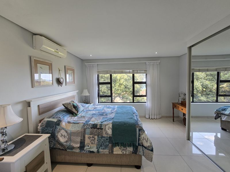 Spacious bedroom featuring tiled flooring, built-in mirrored cupboards, air conditioning, and large windows providing natural light and garden views.