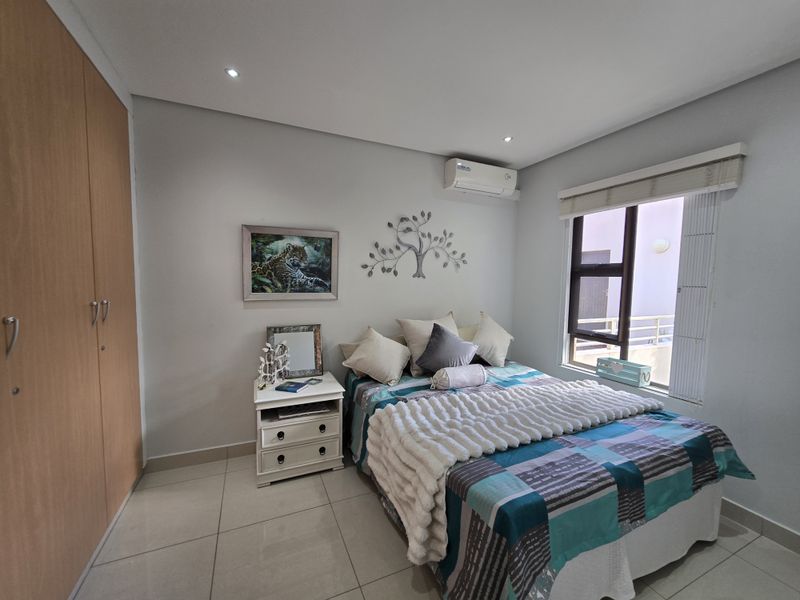 A well-maintained bedroom featuring tiled flooring, built-in cupboards, recessed downlighting, and a wall-mounted air conditioning unit.