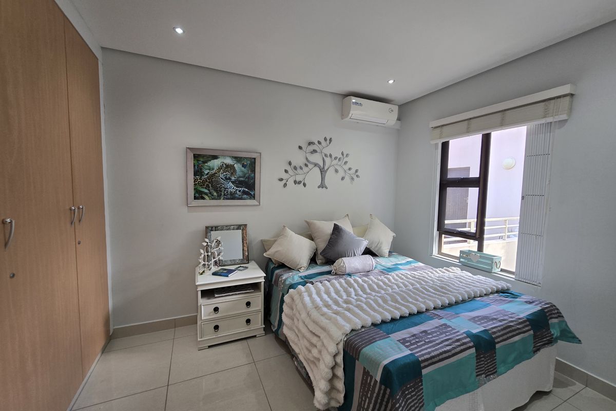 A well-maintained bedroom featuring tiled flooring, built-in cupboards, recessed downlighting, and a wall-mounted air conditioning unit.
