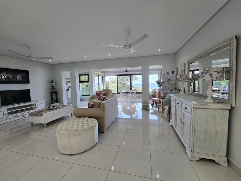 Spacious open-plan living and dining area featuring polished porcelain tiles, recessed lighting, ceiling fans, and large sliding doors with scenic views.