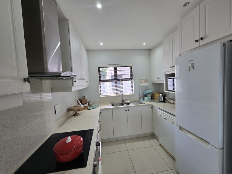 A well-maintained kitchen featuring white cabinetry, stone countertops, integrated appliances, and modern recessed lighting, offering a clean and functional workspace.