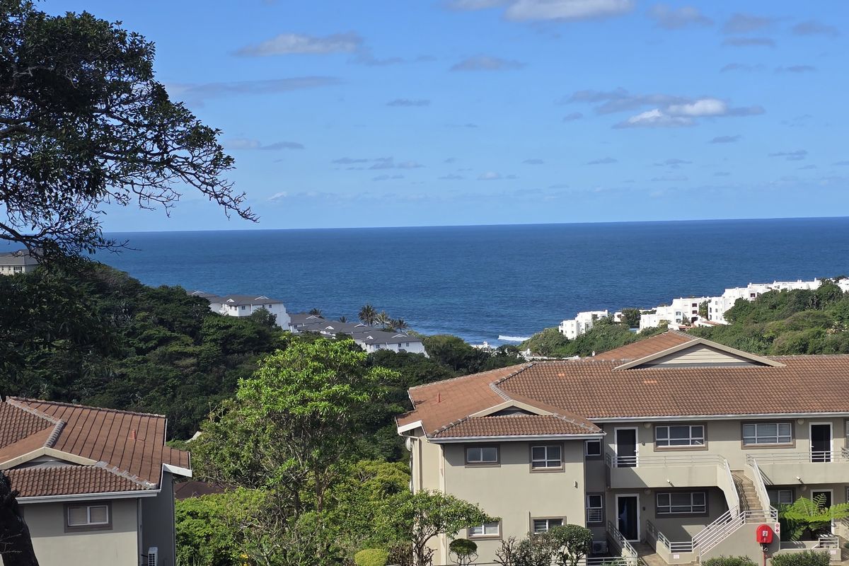 A scenic elevated view overlooking the ocean and surrounding residential apartment complex with tiled roofs and landscaped grounds.