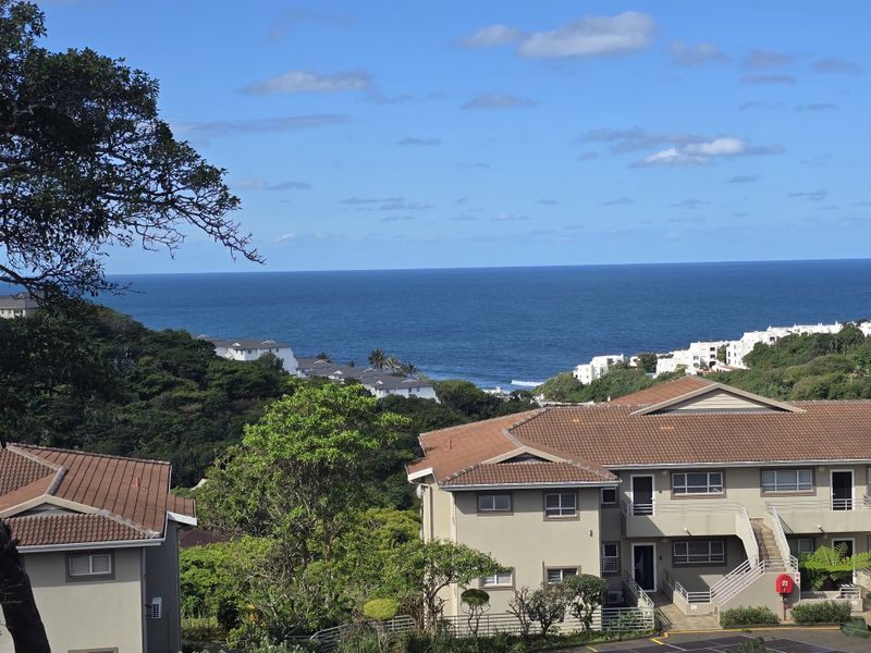 A scenic elevated view overlooking the ocean and surrounding residential apartment complex with tiled roofs and landscaped grounds.