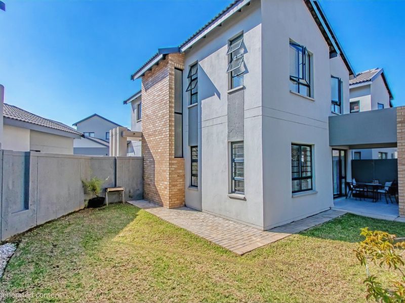 Rear view of a double-storey cluster home featuring a paved patio area, landscaped garden, and modern brick and plaster exterior finishes.