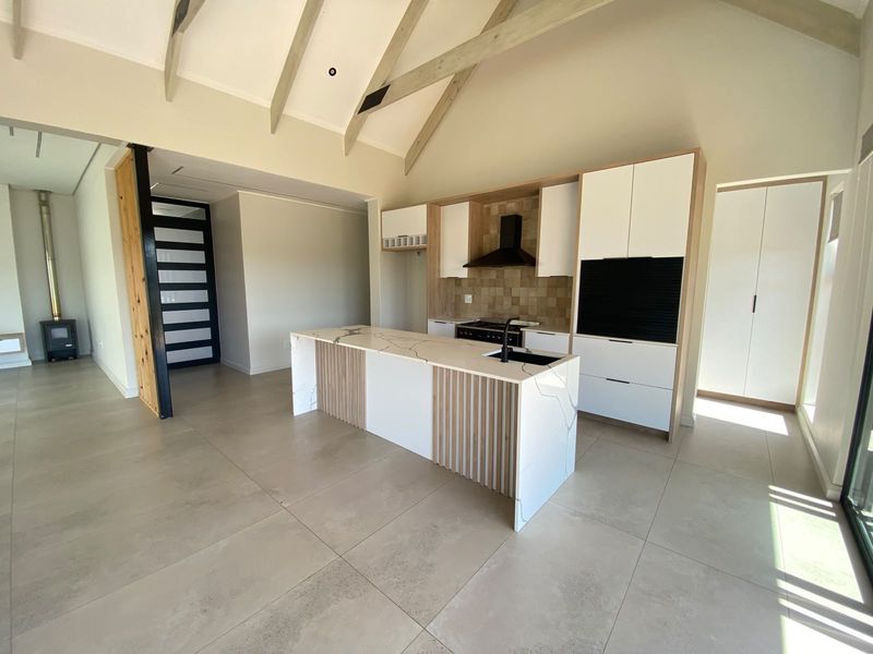 Modern open-plan kitchen featuring a central island with stone countertops, sleek cabinetry, vaulted ceilings with exposed beams, and a cozy fireplace in the adjacent area.