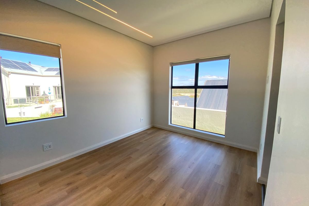 A bright, modern, and empty bedroom featuring high-quality laminate flooring, recessed linear ceiling lighting, and large aluminium-framed windows with natural light.