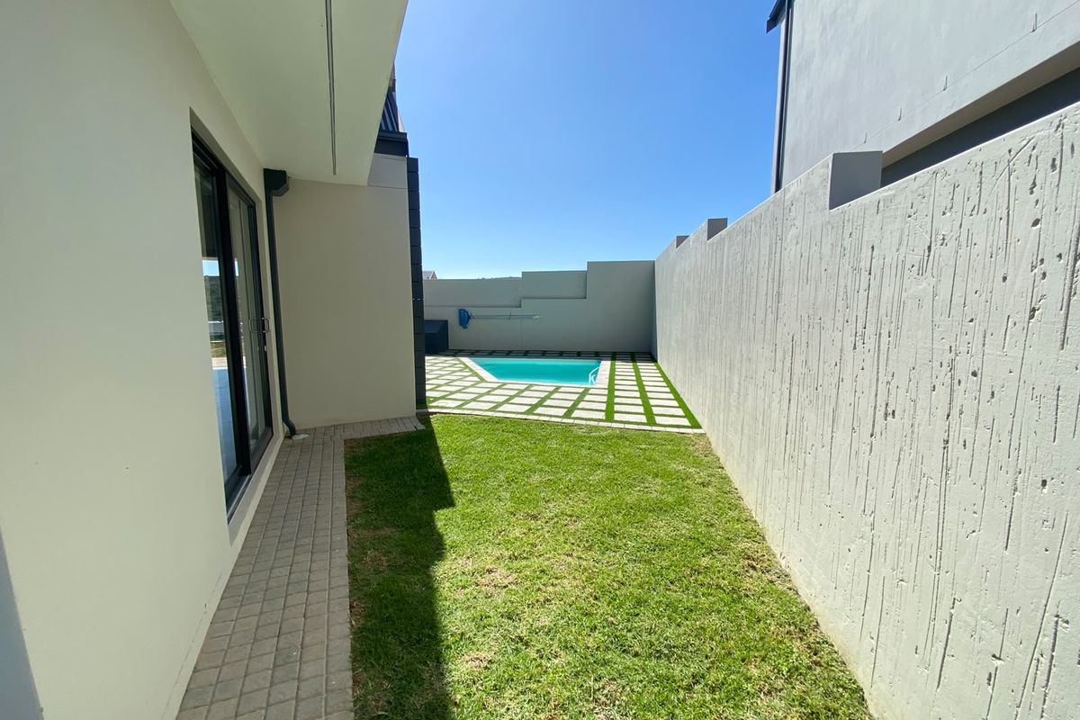 A private rear garden featuring a swimming pool, paved patio area, and a well-maintained lawn enclosed by high boundary walls.