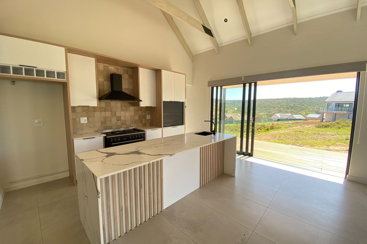 Modern open-plan kitchen featuring a stone-topped island, built-in cabinetry, and vaulted ceilings, with seamless access to an outdoor deck and scenic views.