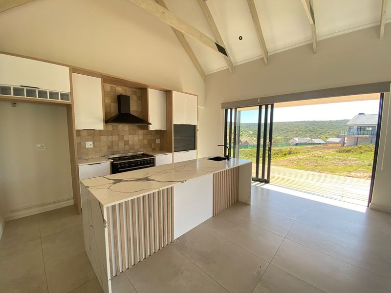 Modern open-plan kitchen featuring a stone-topped island, built-in cabinetry, and vaulted ceilings, with seamless access to an outdoor deck and scenic views.