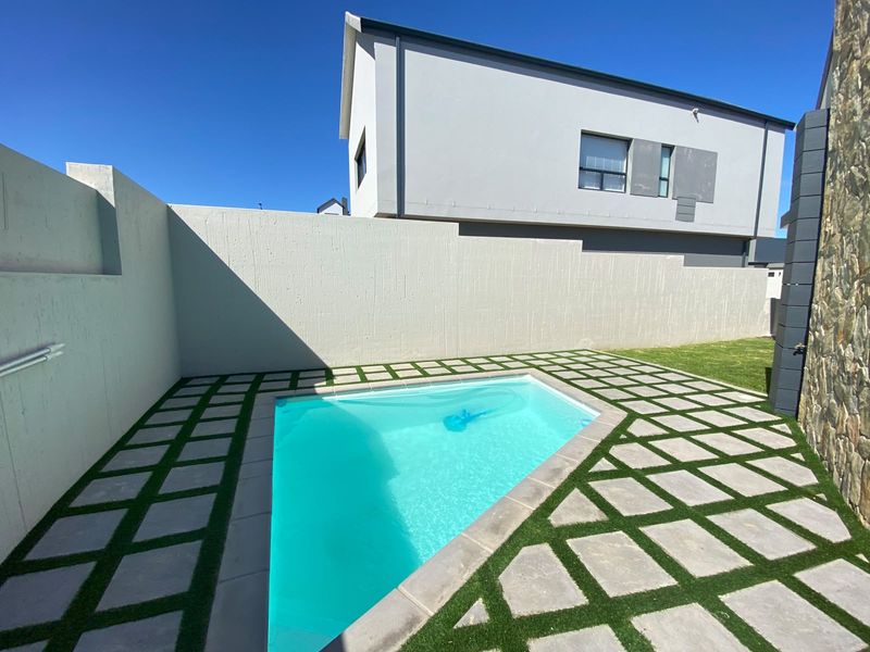 A modern outdoor pool area featuring a clean swimming pool, stone-clad accents, and a contemporary paved patio with integrated artificial grass.