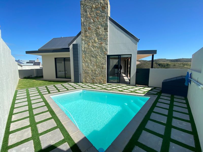 A modern home exterior featuring a swimming pool, stone-clad chimney, and paved patio area with sliding door access to the interior.