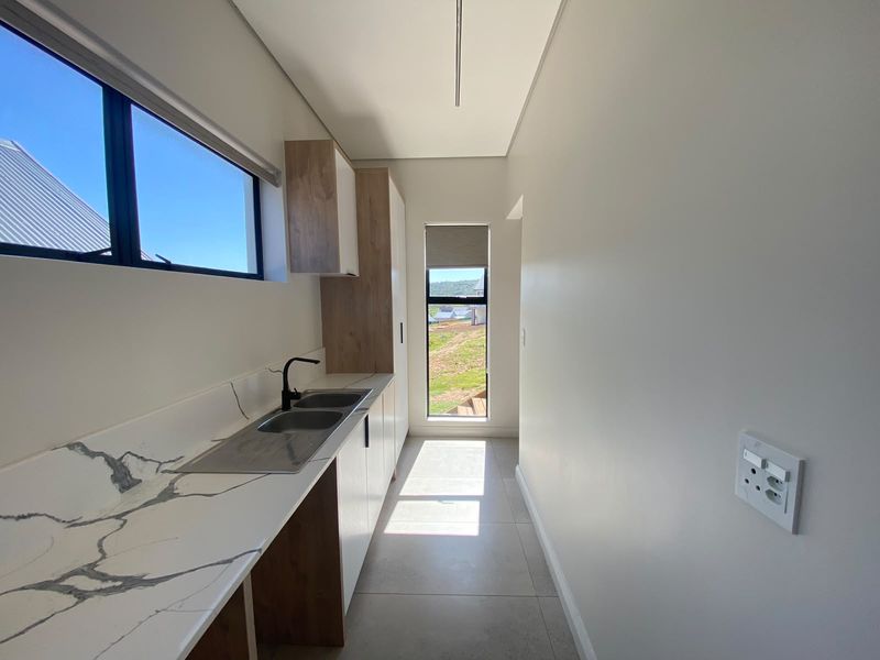 A modern, clean scullery featuring marble-look countertops, double sink, black fixtures, and ample built-in cabinetry with large windows providing natural light.