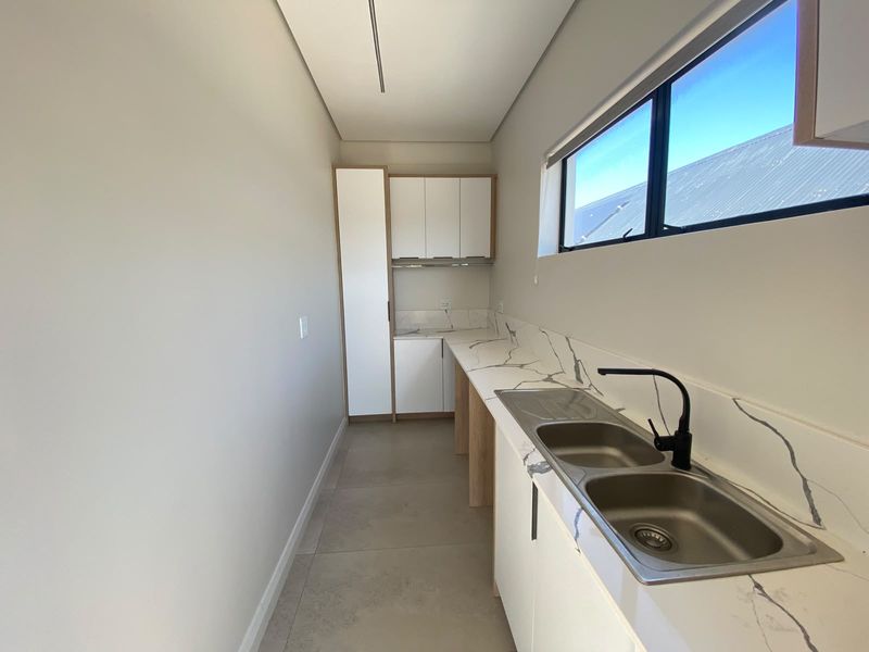 A modern, clean scullery featuring sleek white cabinetry, marble-look stone countertops, a double stainless steel sink with a black mixer tap, and tiled flooring.