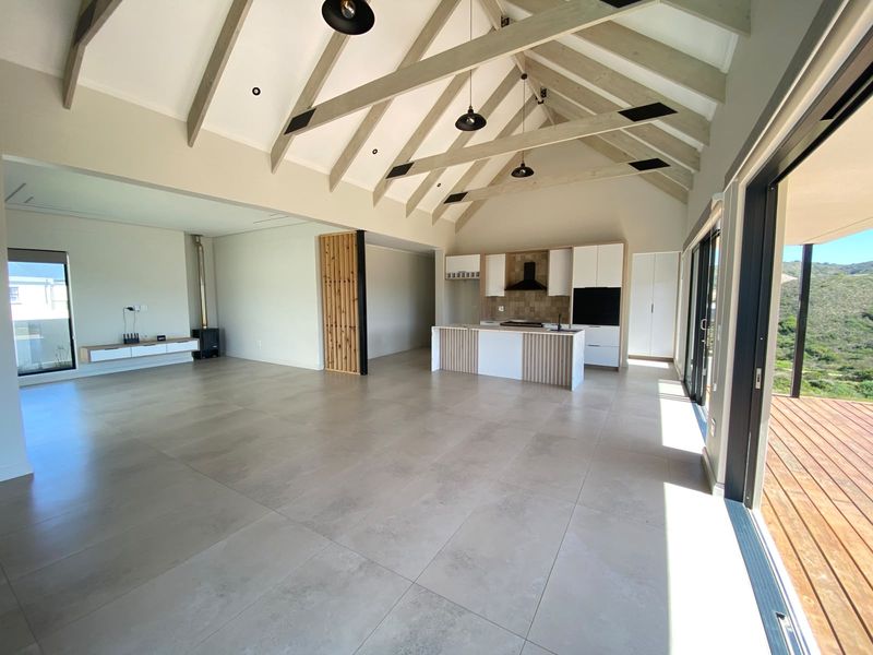 Spacious open-plan living area featuring a vaulted ceiling with exposed beams, modern kitchen with island, and seamless flow to an outdoor timber deck.