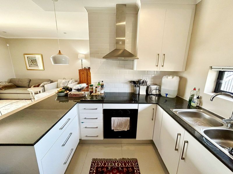 Modern open-plan kitchen featuring white cabinetry, granite countertops, subway tile backsplash, and integrated stainless steel appliances, flowing into the adjacent living area.