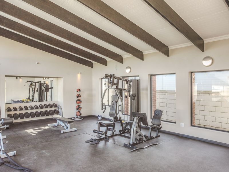 A well-maintained home gym featuring exposed timber ceiling beams, rubberized flooring, and a large wall-mounted mirror, providing a functional space for fitness.