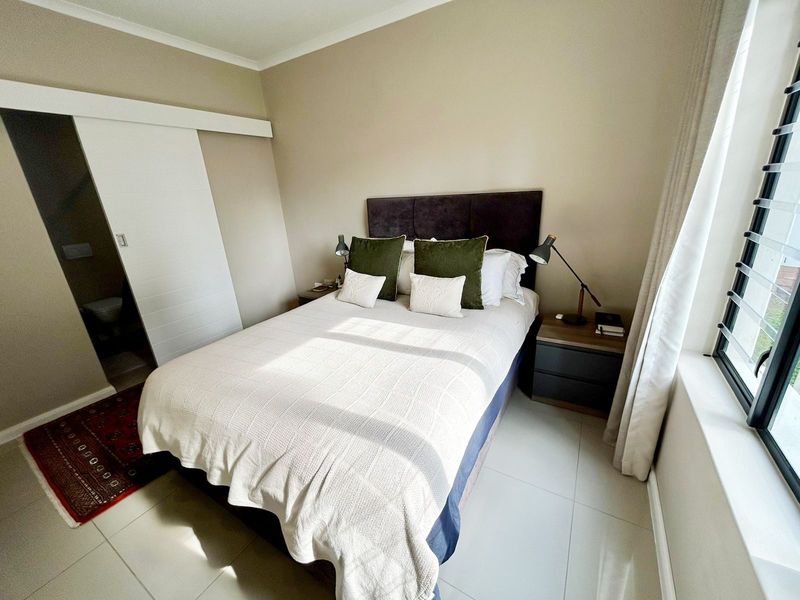 A well-maintained bedroom featuring neutral wall tones, tiled flooring, and a convenient sliding door leading to an en-suite bathroom.