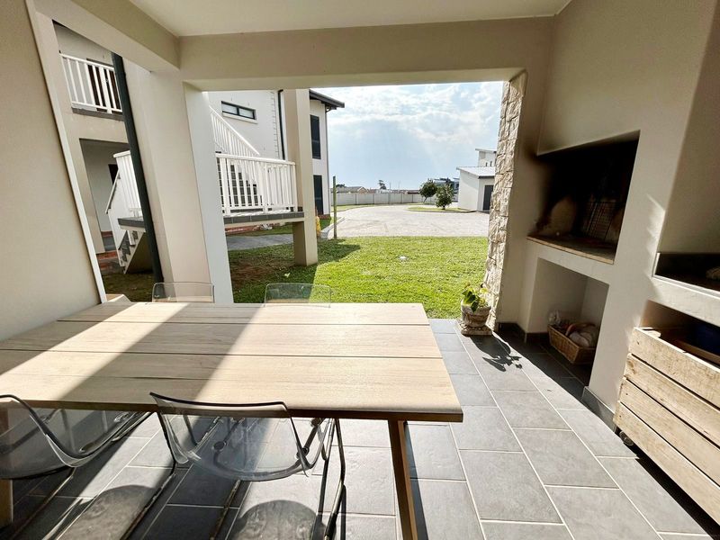 Covered patio area featuring a built-in braai with stone cladding and durable tiled flooring, overlooking a communal garden space.