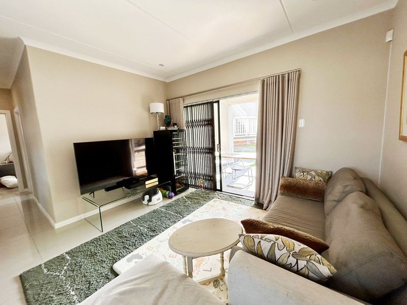 A well-maintained living room featuring tiled flooring, cove cornicing, and a sliding glass door with a security gate leading to an outdoor patio area.