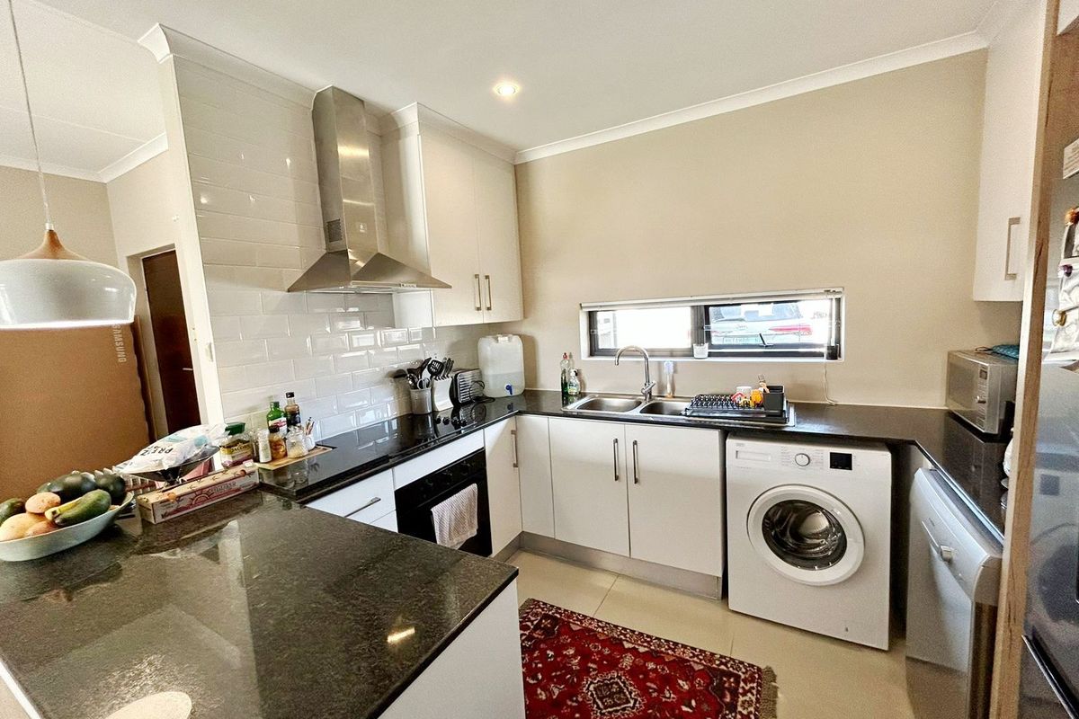 Modern kitchen featuring white cabinetry, dark granite countertops, subway tile backsplash, stainless steel extractor fan, and integrated laundry appliances.