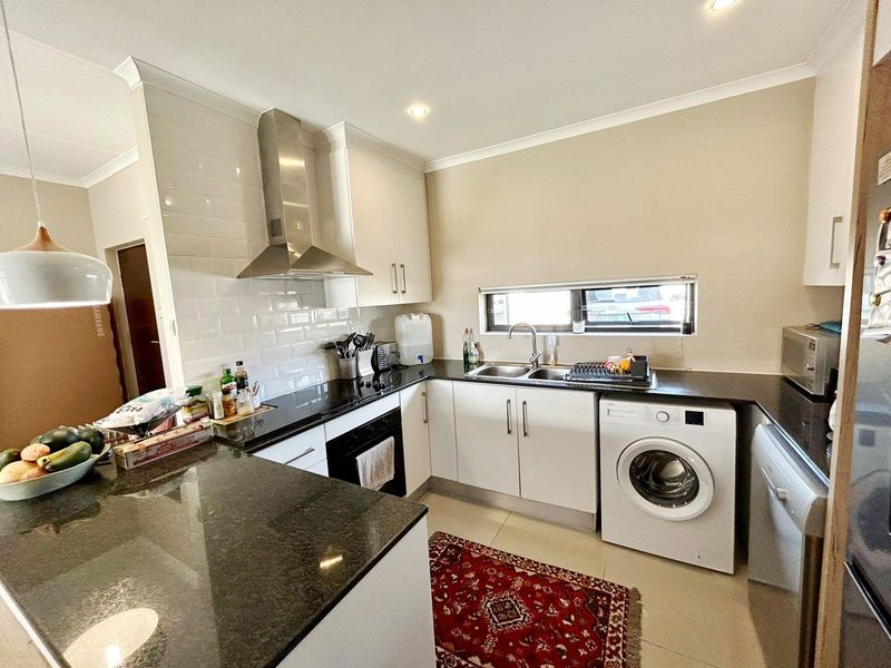 Modern kitchen featuring white cabinetry, dark granite countertops, subway tile backsplash, stainless steel extractor fan, and integrated laundry appliances.