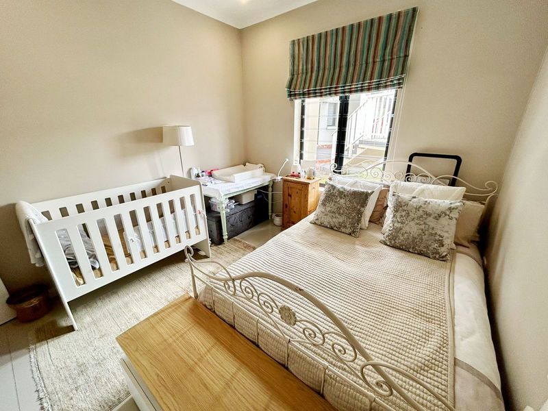 A functional bedroom featuring neutral wall tones, a window with security bars, and a Roman blind.