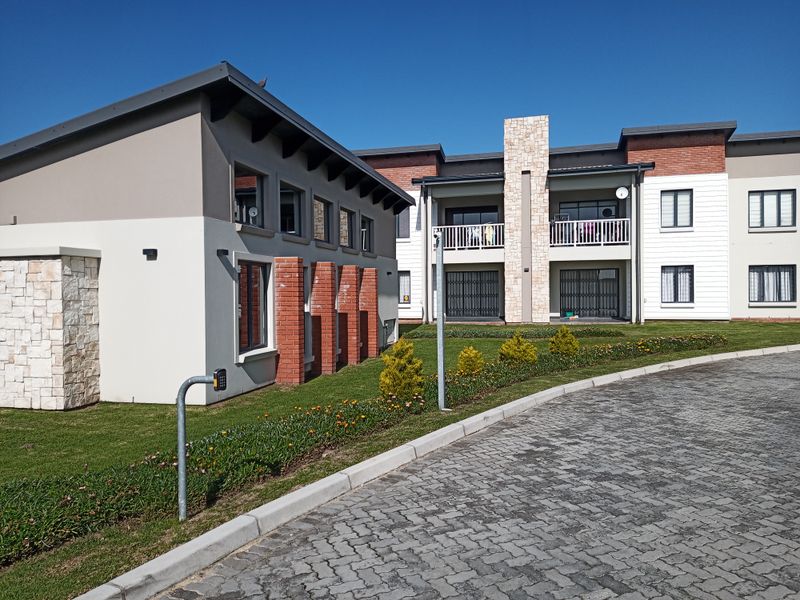 Modern apartment complex exterior featuring stone and brick accents, well-maintained lawns, paved driveway, and private balconies with security gates.