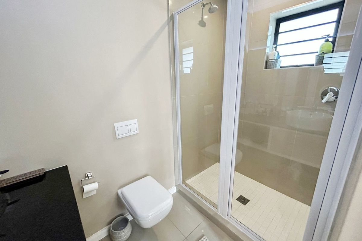 A modern, clean bathroom featuring a wall-mounted toilet, a glass-enclosed shower with tiled flooring, and a sleek vanity countertop.