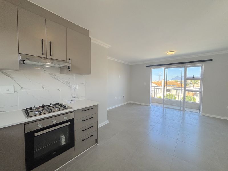 Modern open-plan kitchen and living area featuring sleek cabinetry, built-in appliances, tiled floors, and direct access to a balcony with scenic views.