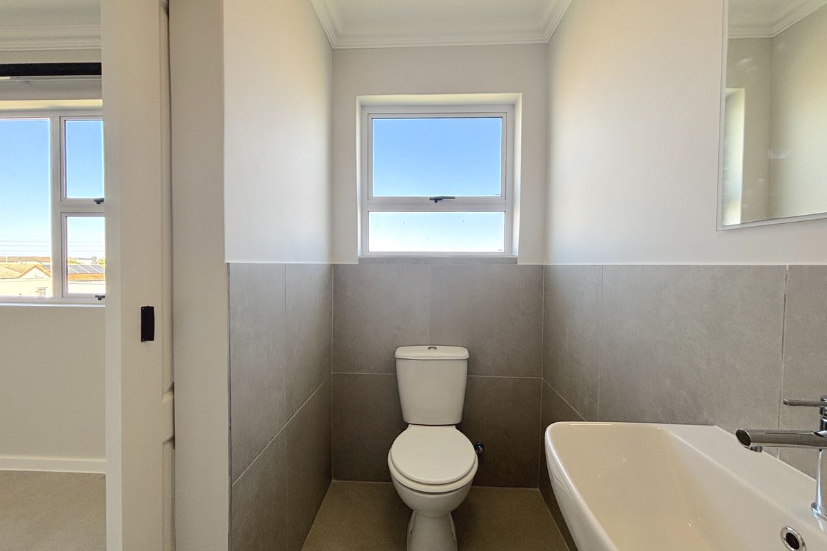A clean and modern bathroom featuring neutral wall and floor tiles, a white toilet, and a wall-mounted washbasin with a chrome mixer tap.