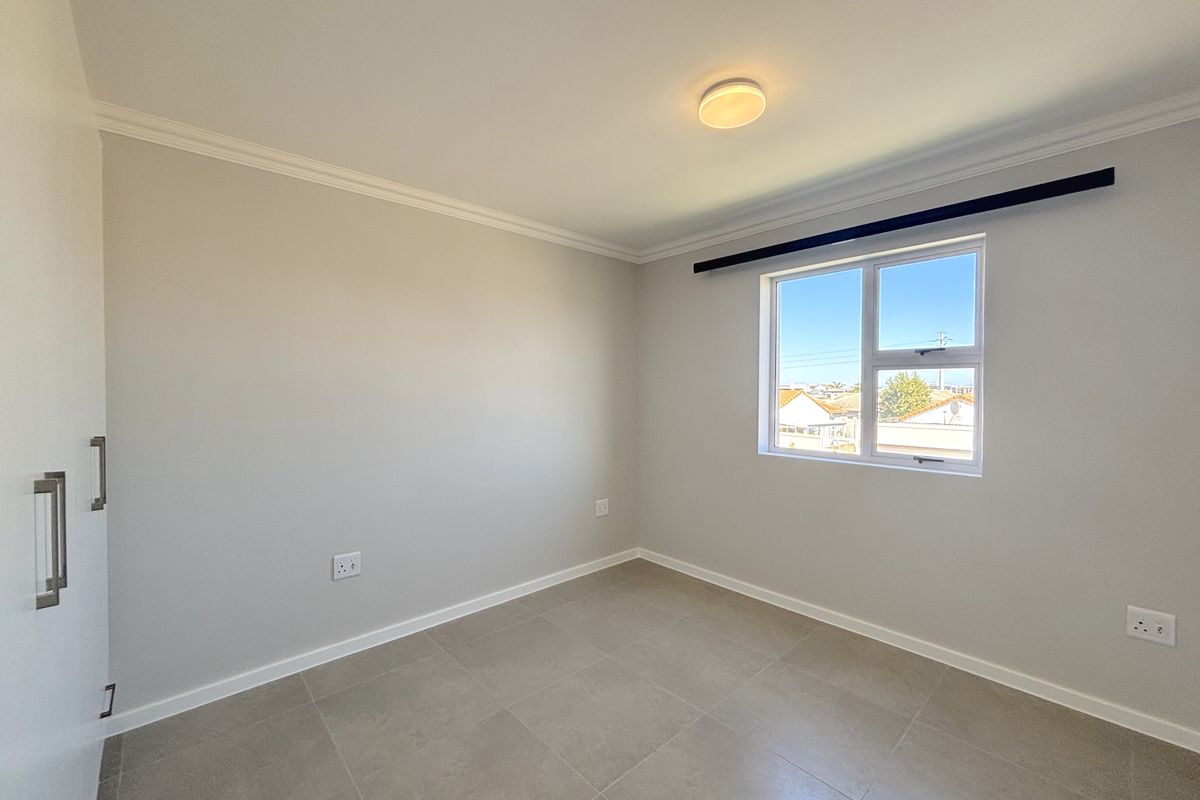 A bright, empty bedroom featuring neutral tiled flooring, built-in cupboards, and a window with natural light.