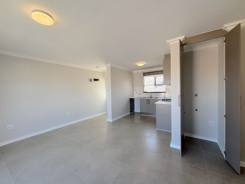 An open-plan living and kitchen area featuring neutral tiled flooring, modern cabinetry, a gas hob, and a dedicated built-in storage cupboard.