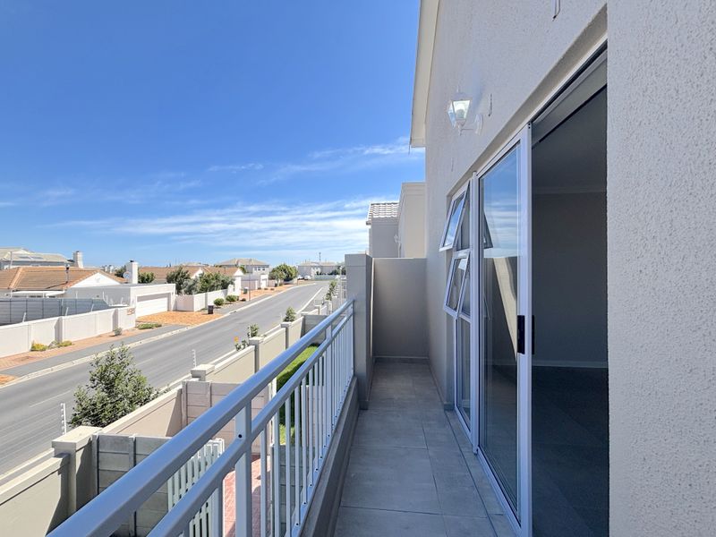A clean, modern balcony featuring tiled flooring, a secure metal balustrade, and sliding glass door access to the interior living space.