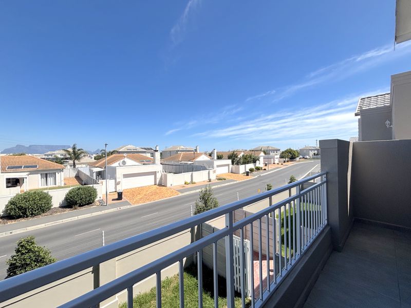 A clean, elevated balcony featuring a metal balustrade and tiled flooring, offering an open view of the surrounding residential street and neighbourhood.