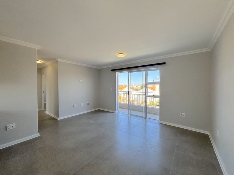 A bright, spacious, and empty living area featuring neutral tiled floors, modern finishes, and direct access to a private balcony through sliding glass doors.